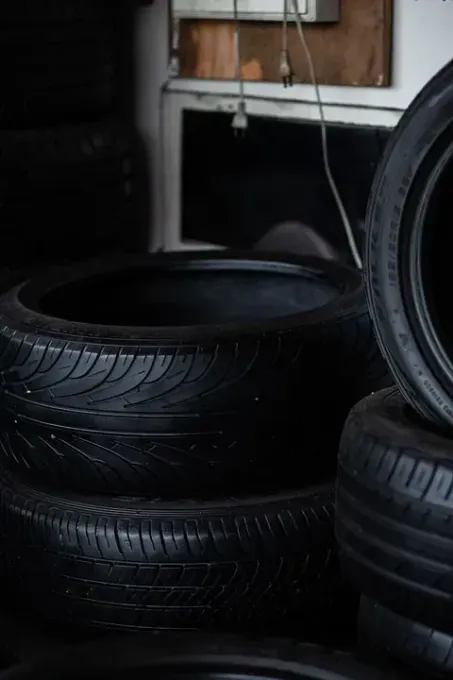 Una pila de neumáticos de goma negra en un taller o garaje, con algunos neumáticos borrosos en primer plano y al fondo.