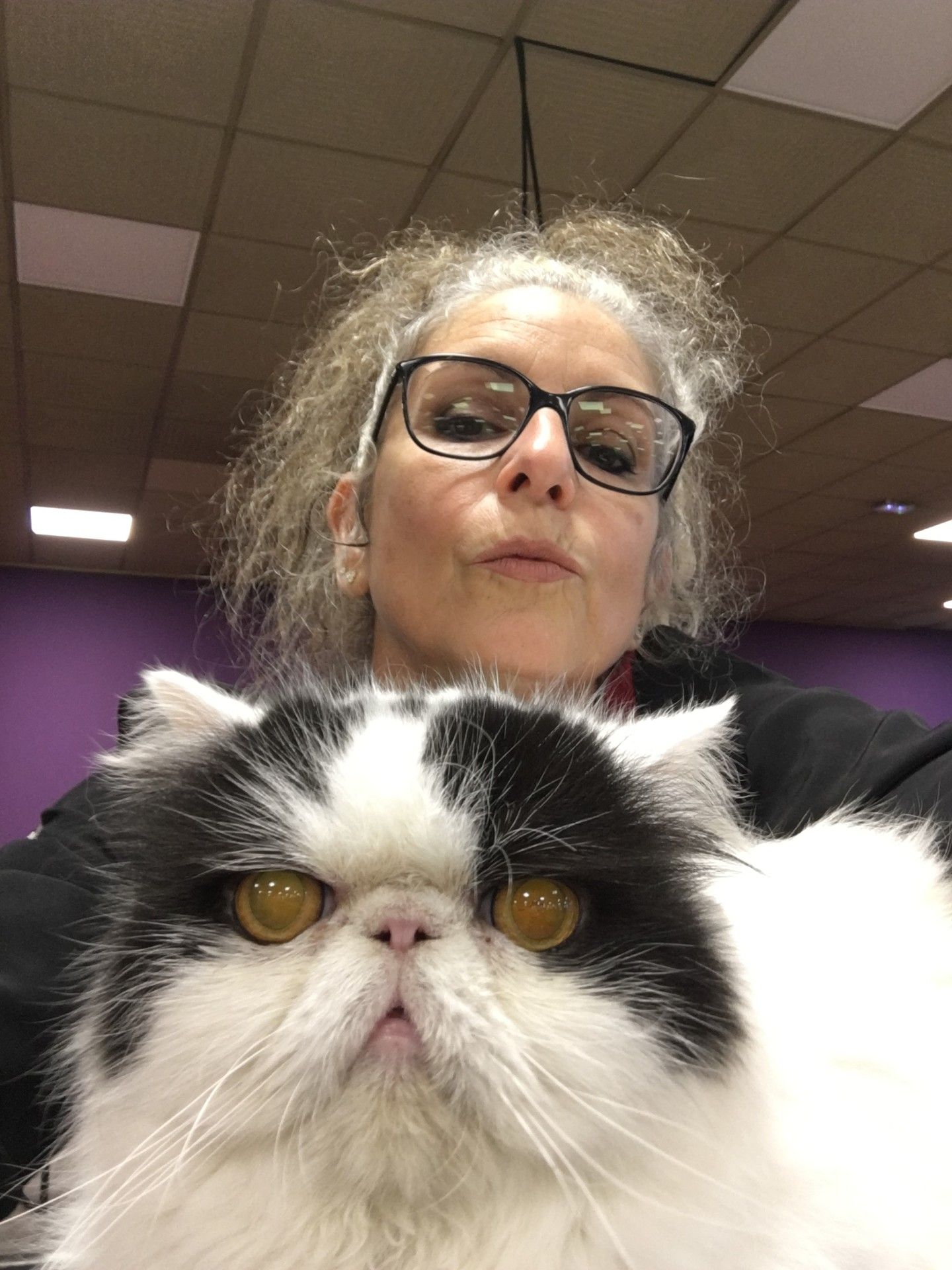 Une femme portant des lunettes avec un chat noir et blanc ; toutes deux regardent l'objectif.