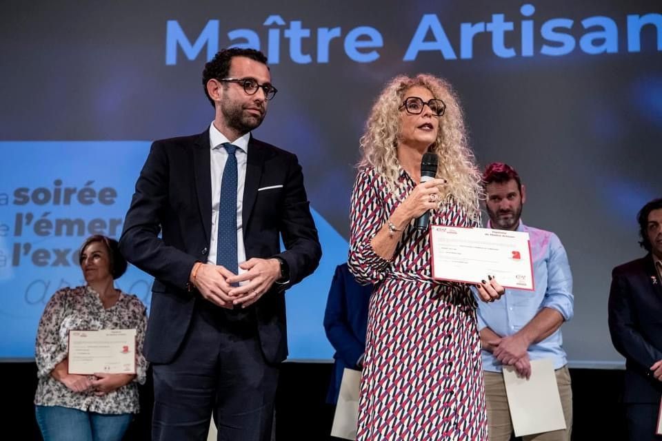 Une femme parle au micro, tenant un certificat, aux côtés d'un homme en costume lors d'une cérémonie de remise de prix.