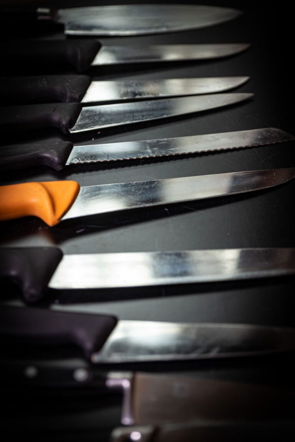 Reihe von Küchenmessern mit schwarzen Griffen, ausser einem mit orangefarbenem Griff.