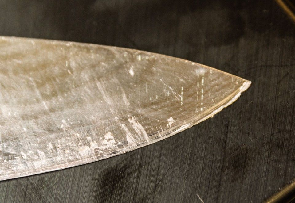 Nahaufnahme einer stumpfen Metallmesserklinge auf einer dunklen Oberfläche mit Kratzern und Abnutzung.