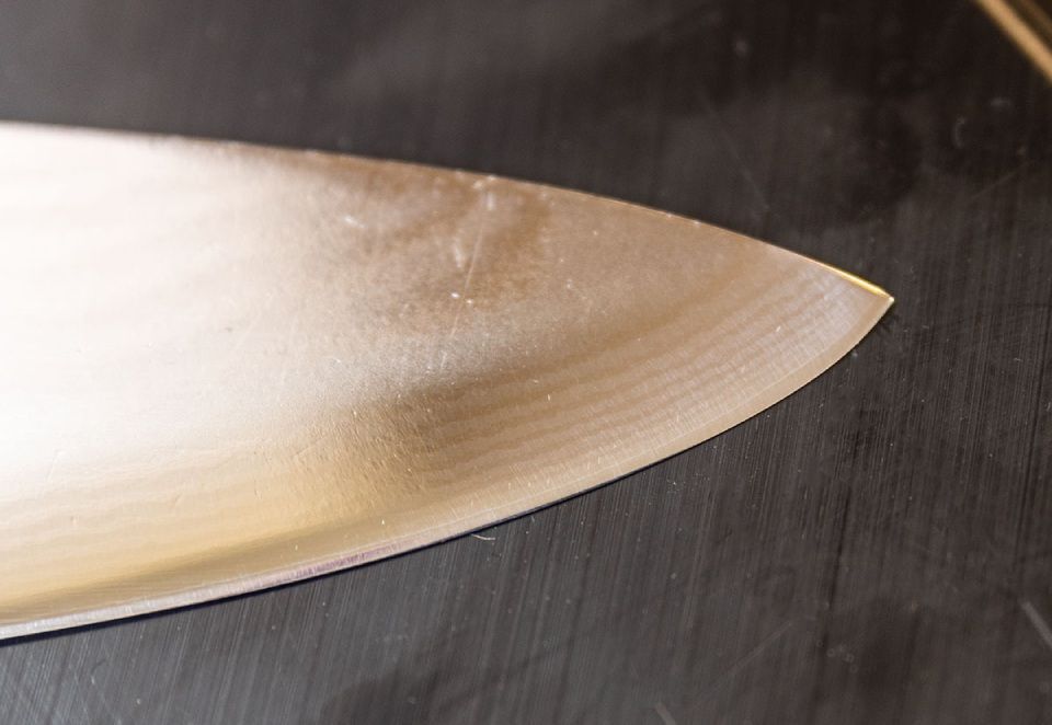 Nahaufnahme einer glänzenden, silbernen Messerklinge auf einer dunklen Oberfläche, die Spitze und Schneide zeigt.