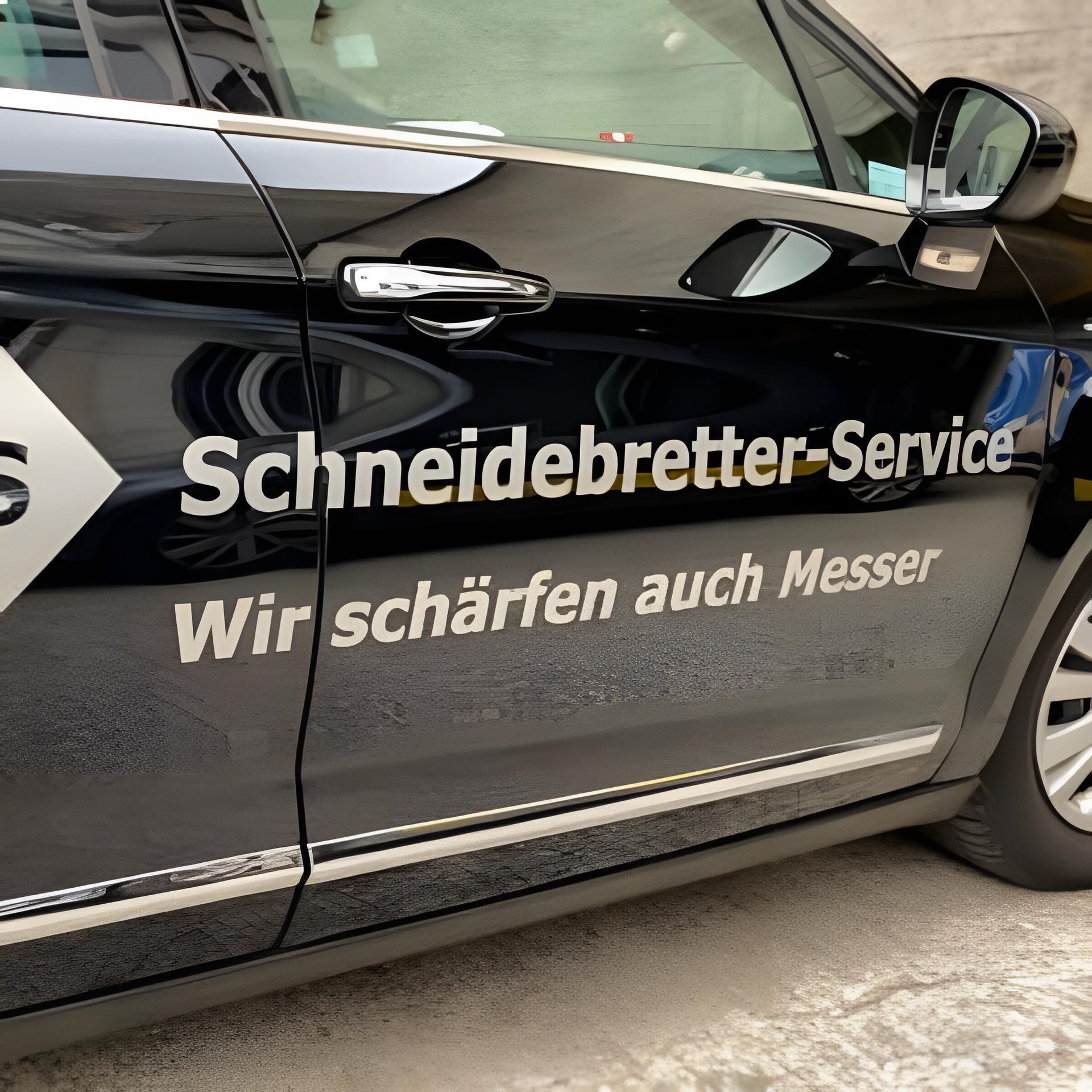Schwarzes Auto mit seitlichem Schriftzug „Schneidebretter-Service“ und „Wir schärfen auch Messer“ in weisser Schrift.