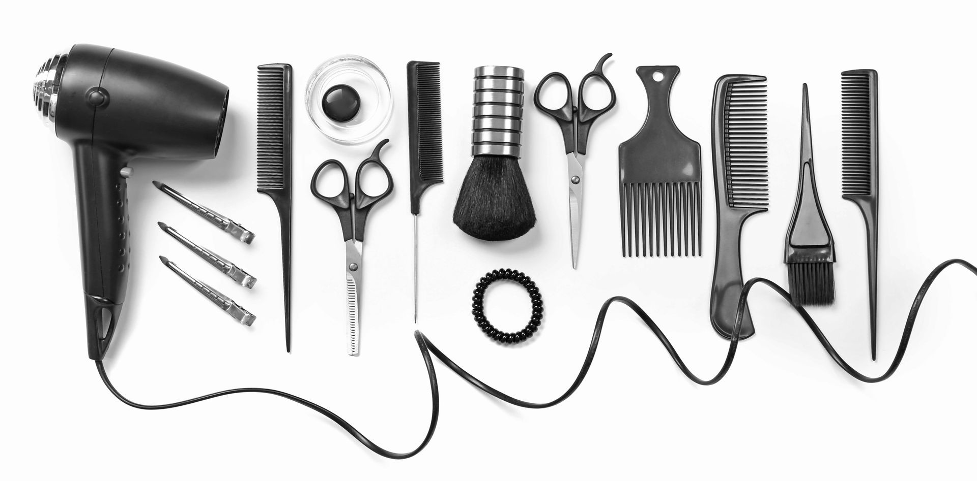 Des outils de coiffure disposés sur une surface blanche, notamment un sèche-cheveux, des peignes et des ciseaux.