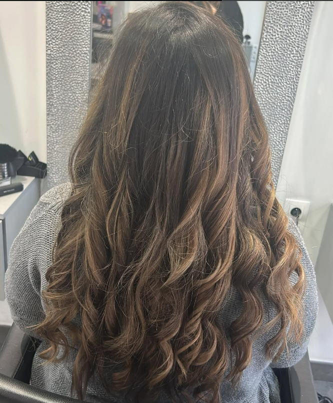 Femme aux longs cheveux bruns ondulés avec des mèches, coiffée dans un salon de coiffure.