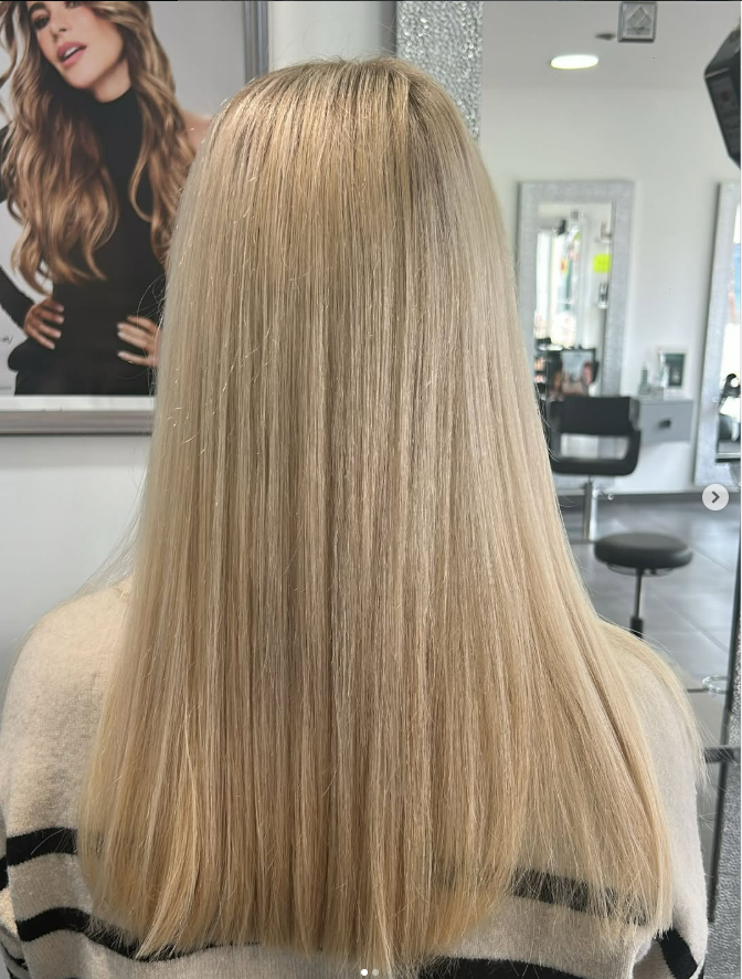 Cheveux blonds, raides et longs, dans un salon de coiffure. La personne est de dos et porte un pull.