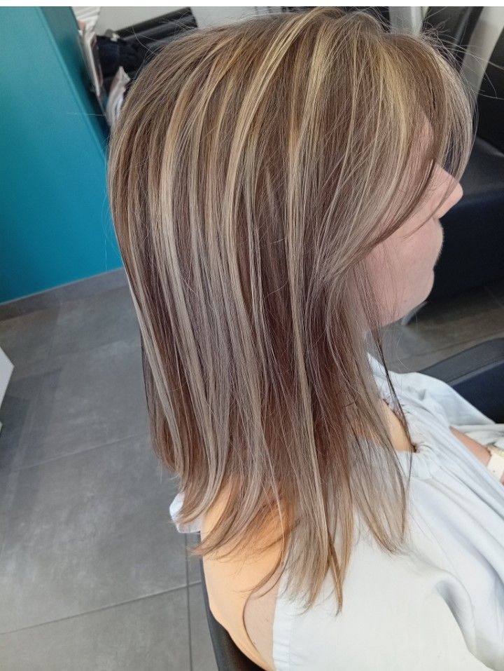 Femme aux cheveux châtain clair, avec des mèches et une coupe dégradée, dans un salon de coiffure.