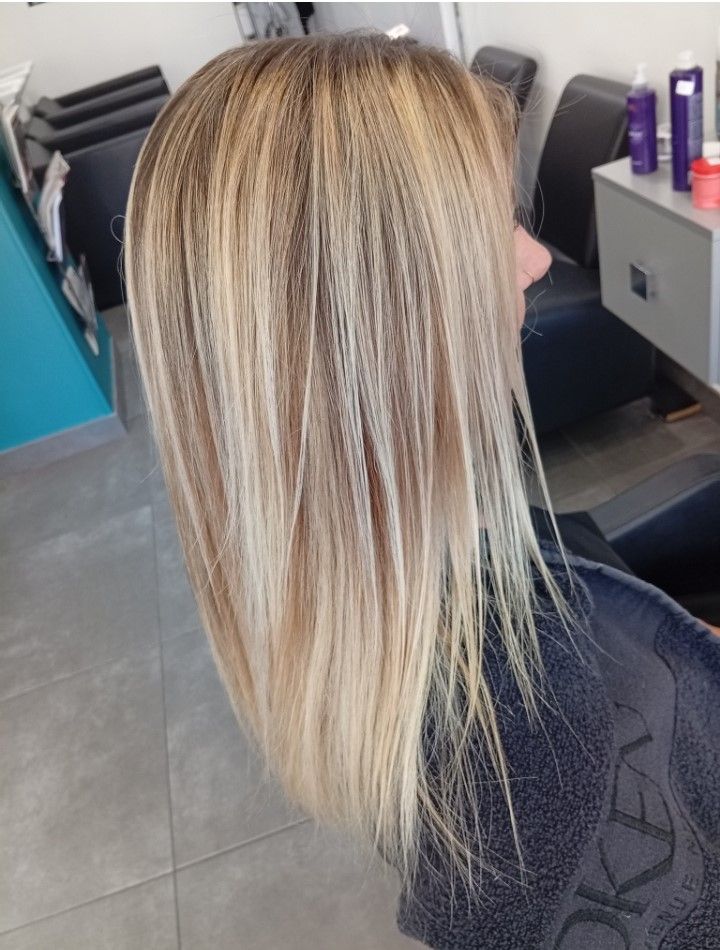 Cheveux blonds avec des racines plus foncées, lissés. Dans un salon de coiffure.