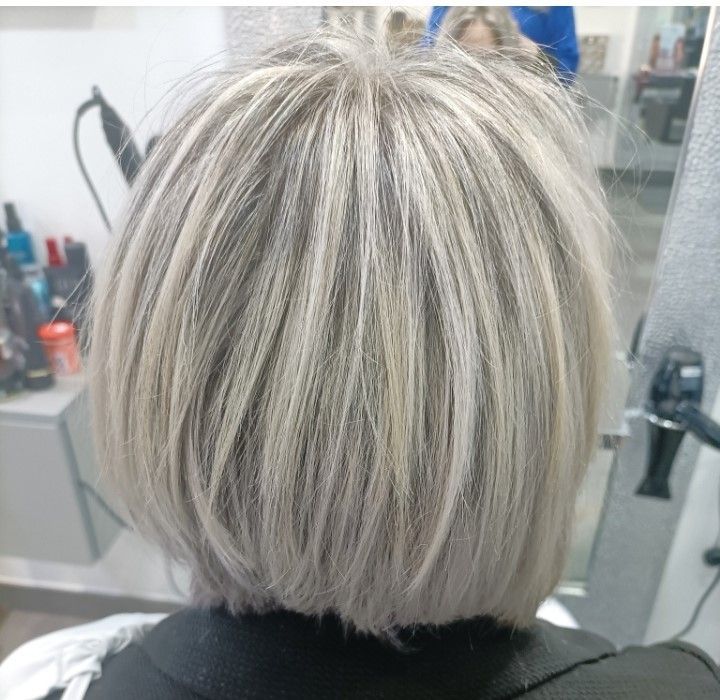 Vue de dos d'une personne aux cheveux courts, dégradés, blond cendré avec des mèches, dans un salon de coiffure.