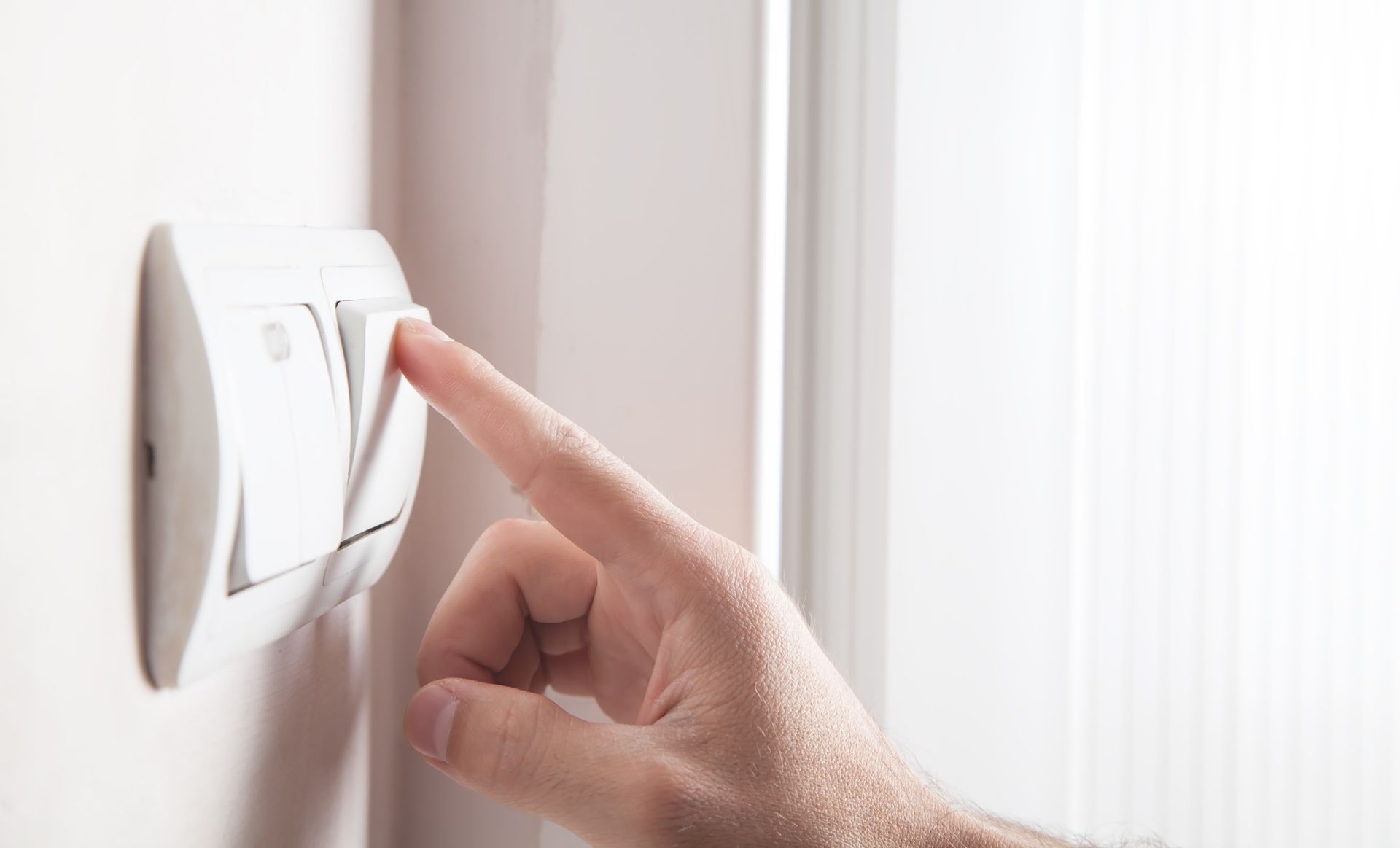 Une main actionne un interrupteur sur un mur blanc.