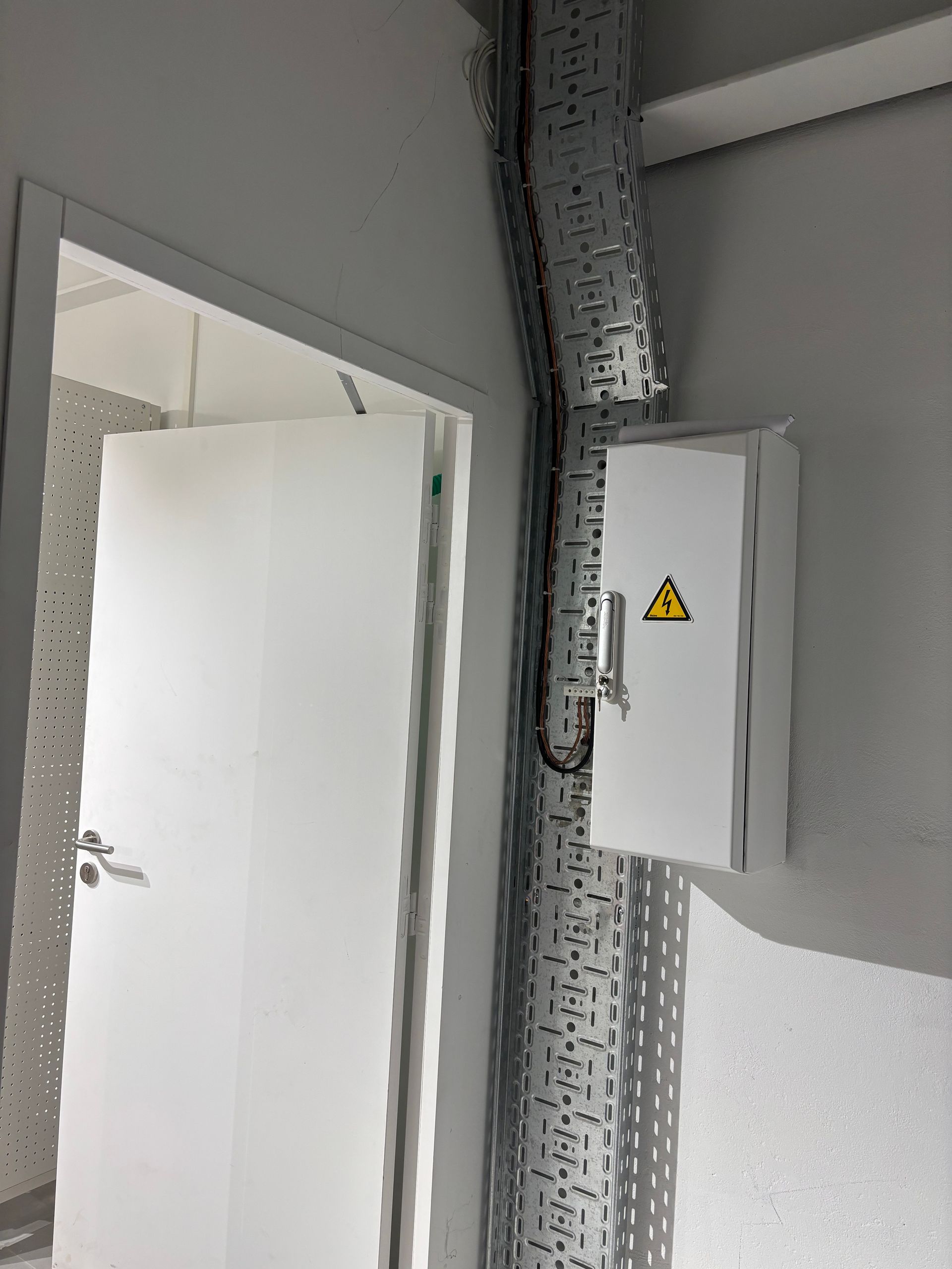 Porte blanche et boîte électrique avec panneau d'avertissement haute tension. Chemin de câbles métallique le long du mur.