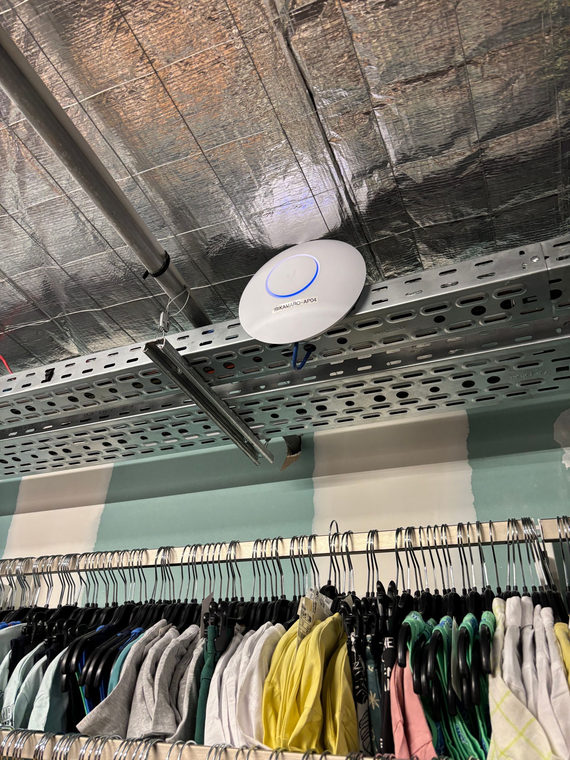 Point d'accès Wi-Fi fixé au plafond dans un magasin de détail avec des portants à vêtements en dessous.