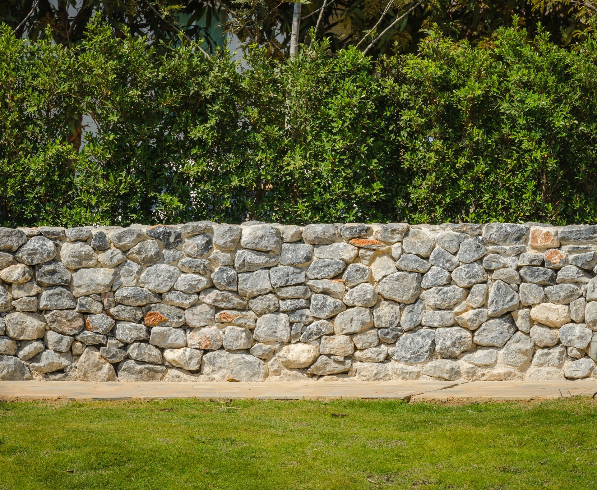 Mur en pierre recouvert de végétation verte et pelouse devant.