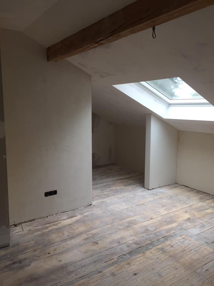 Intérieur d'une pièce en construction avec cloisons sèches, moulures et grande fenêtre.