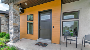 Extérieur d'une maison moderne avec une porte sombre, de petites fenêtres et un pilier en pierre.