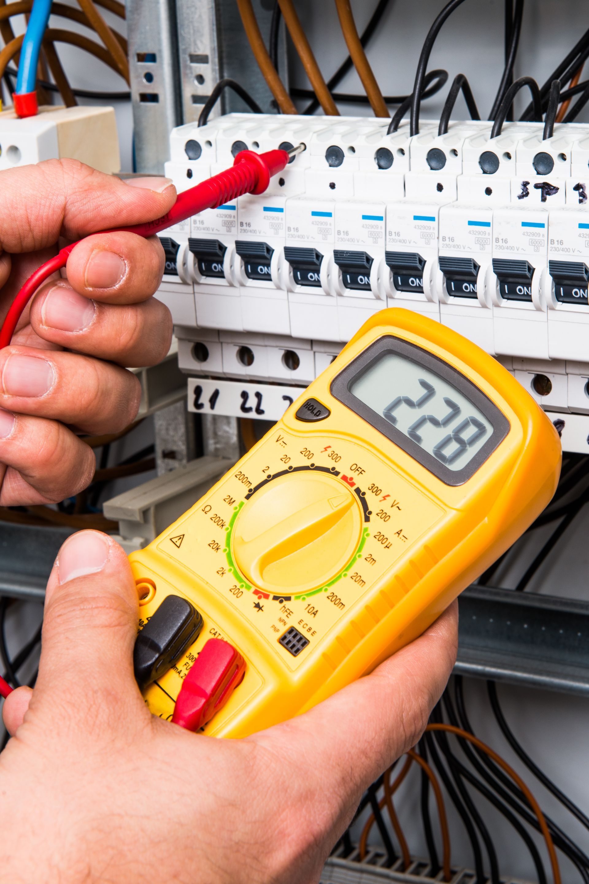 Un électricien utilise un multimètre pour mesurer la tension dans un boîtier de disjoncteur, indiquant 228 volts.