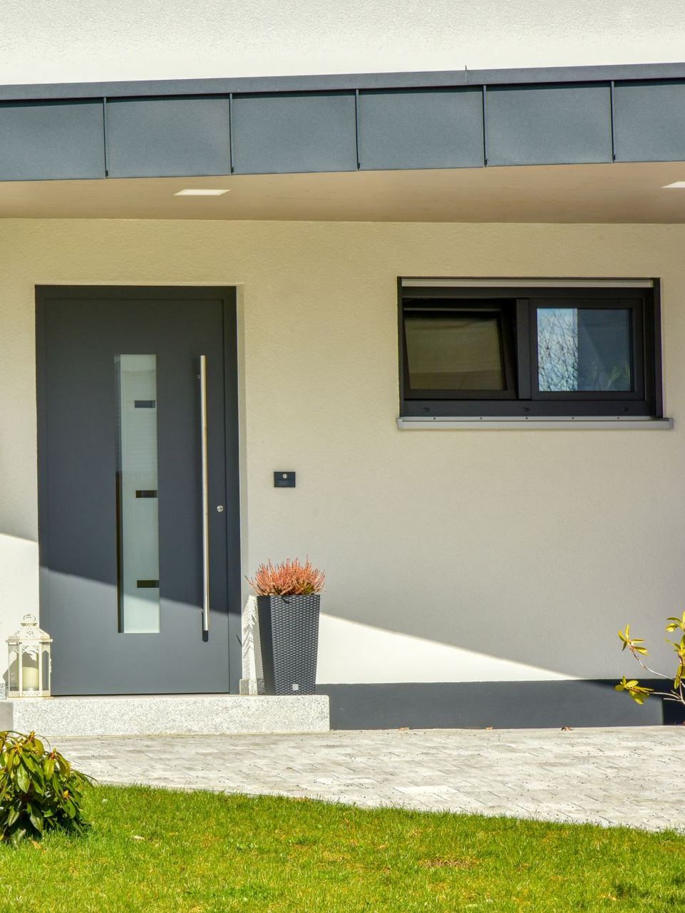 Porte d'entrée grise avec panneau en verre et longue poignée, extérieur de maison moderne.