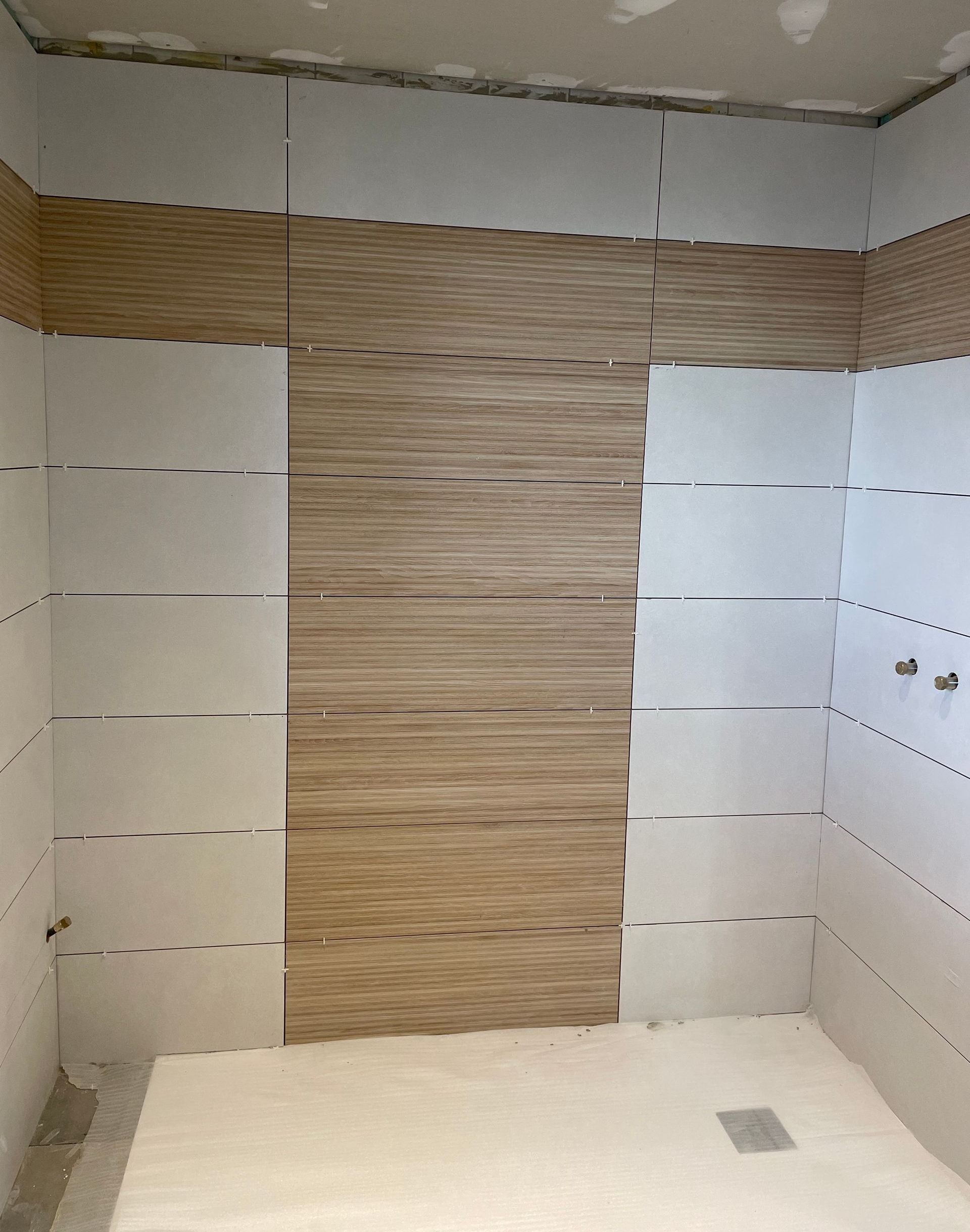 Douche en cours de réalisation, carrelée de carreaux blancs et à motifs imitation bois.