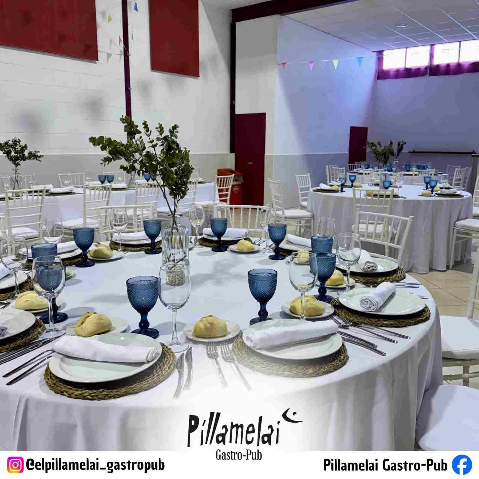 Mesas redondas para banquetes, dispuestas con cristalería azul y bajoplatos dorados en un salón de eventos blanco.
