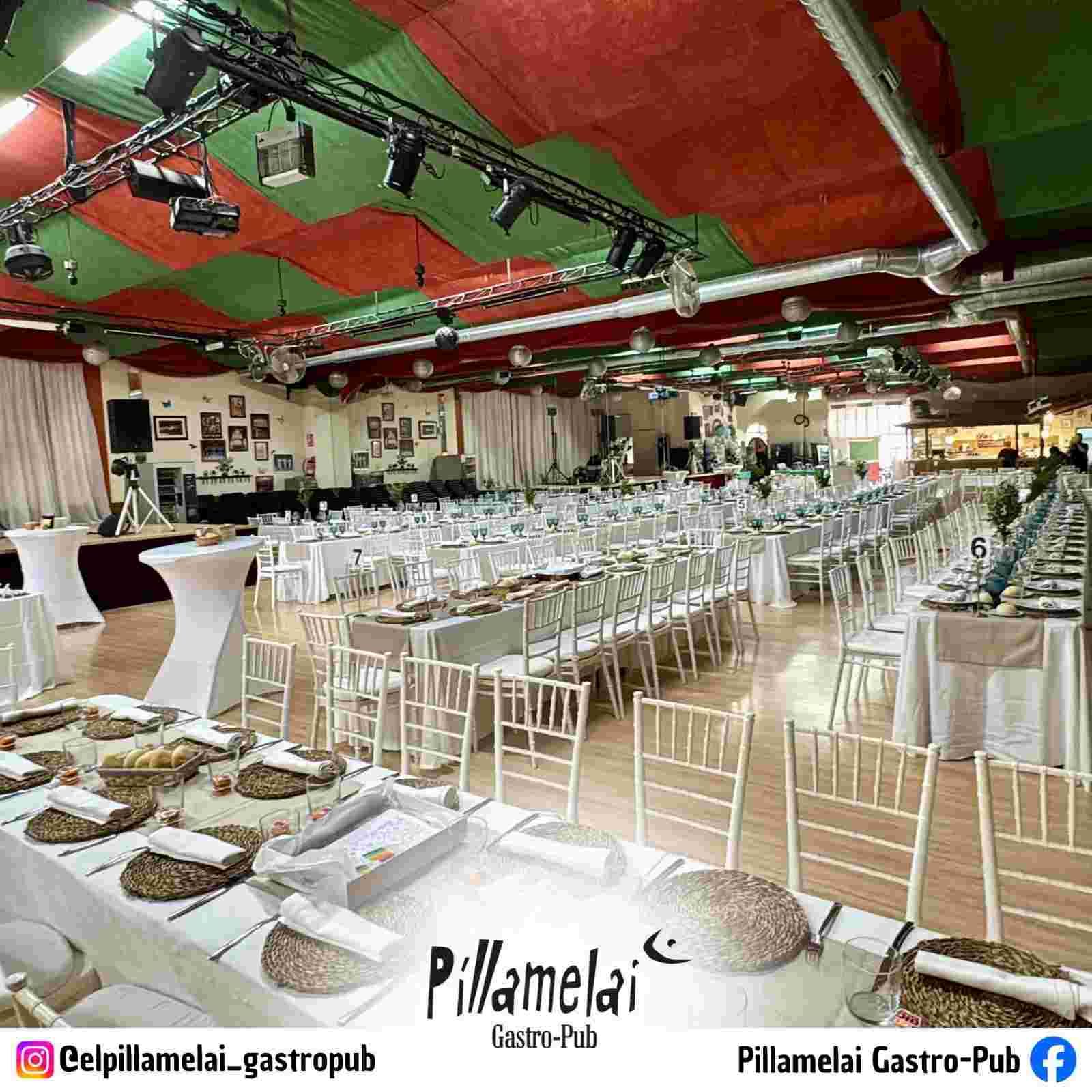 Elegante salón de banquetes con sillas blancas, mesas largas y un techo rojo y verde decorado para un evento.