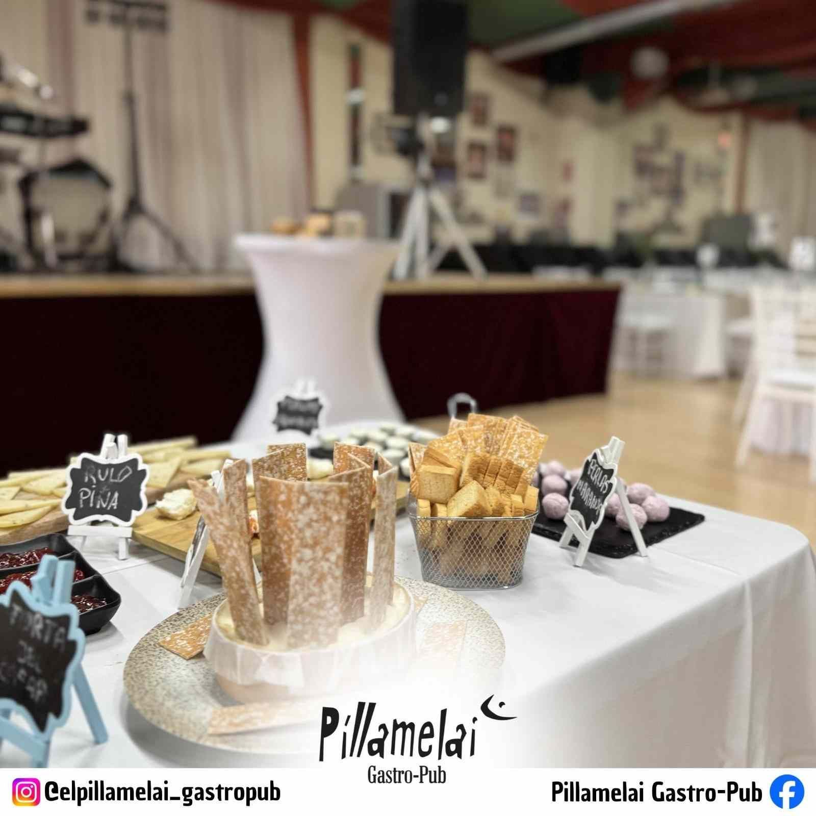 Mesa de postres con pasteles y tartas variadas sobre un mantel blanco en un salón de eventos interior.