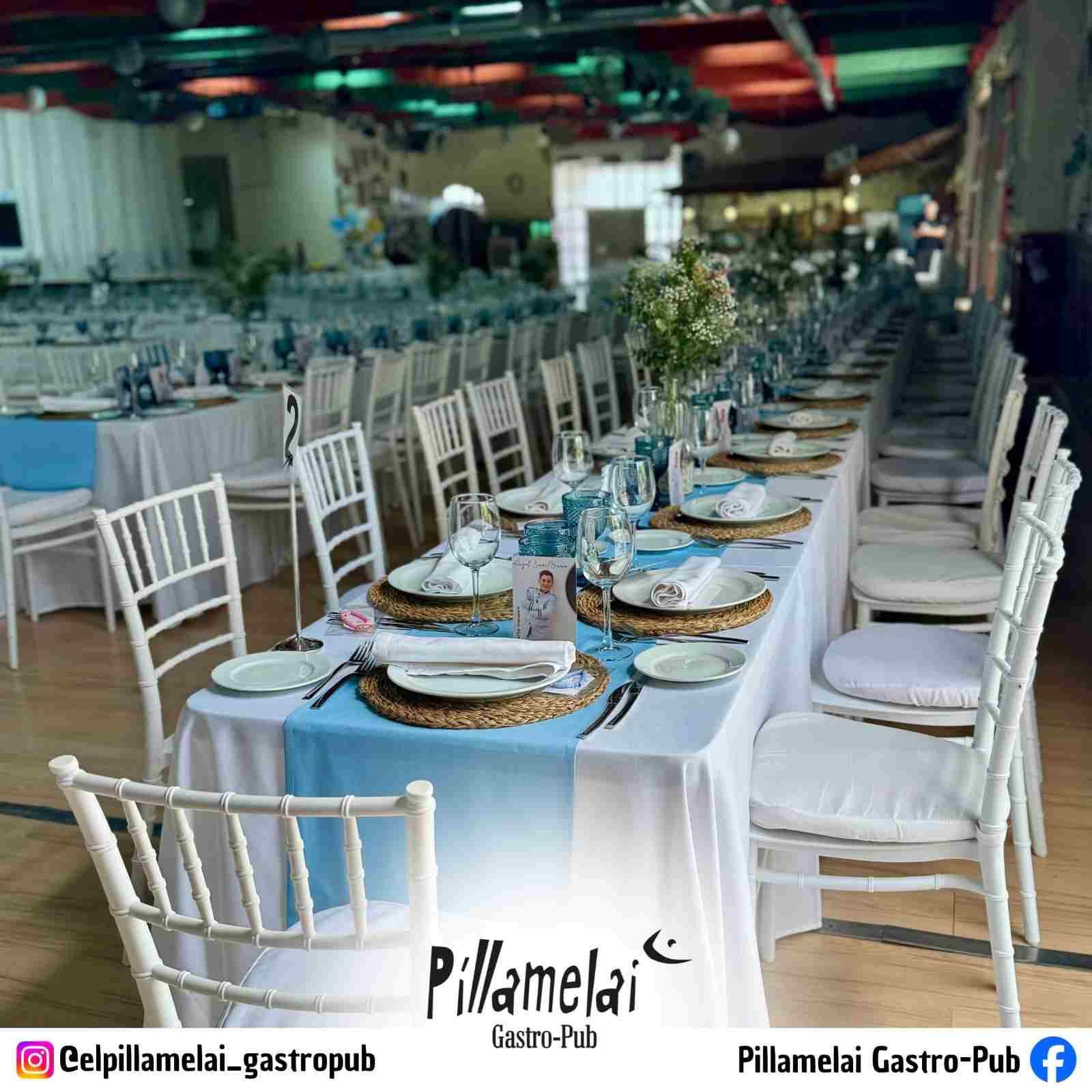 Largas mesas de banquete dispuestas con manteles azules y sillas blancas en un elegante espacio interior.