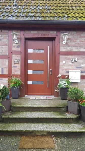 Die Haustür eines Hauses mit Treppen und Topfpflanzen davor.