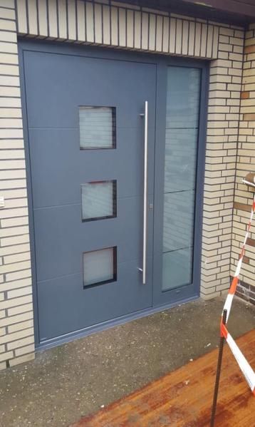 Vor einem Backsteingebäude befindet sich eine graue Tür mit drei Quadraten darauf.