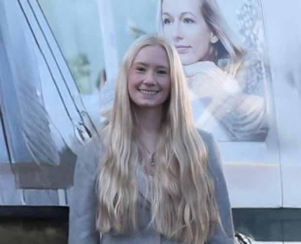 Lächelnde blonde Frau vor einer Außenwerbung mit einer Frau.