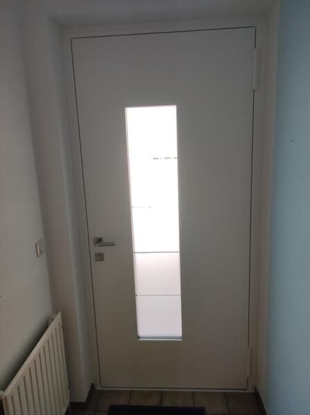 Eine weiße Tür mit einem Fenster und einem Heizkörper in einem Flur.