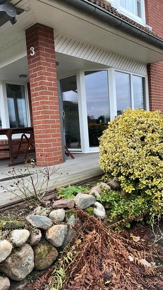 Ein Backsteinhaus mit einer Terrasse und einem Busch davor.