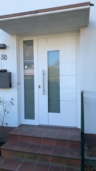 Eine weiße Haustür mit einem Vordach darüber und einer Treppe, die dorthin führt.