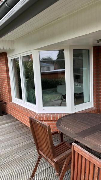 Auf der Terrasse vor einem großen Fenster stehen ein Tisch und Stühle.
