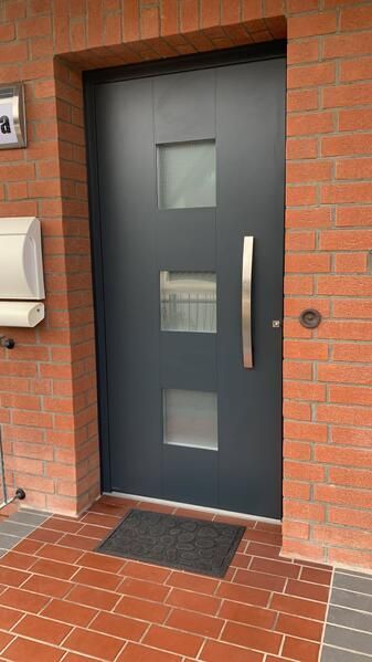 Eine schwarze Tür befindet sich an einer Backsteinmauer neben einem Briefkasten.