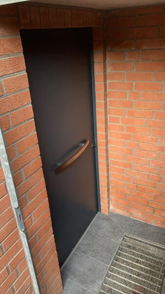 Neben einer Backsteinmauer steht eine schwarze Tür.