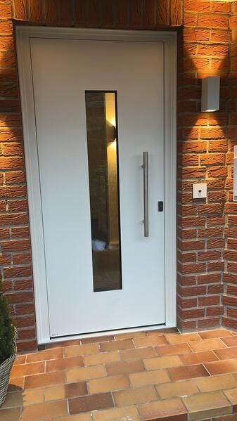 An einer Backsteinmauer befindet sich eine weiße Tür mit einem Glasfenster.