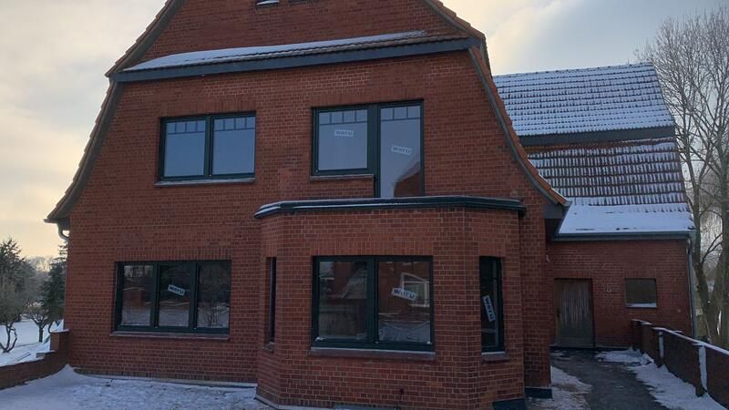 Ein großes rotes Backsteinhaus mit schwarzen Fenstern ist von Schnee umgeben.