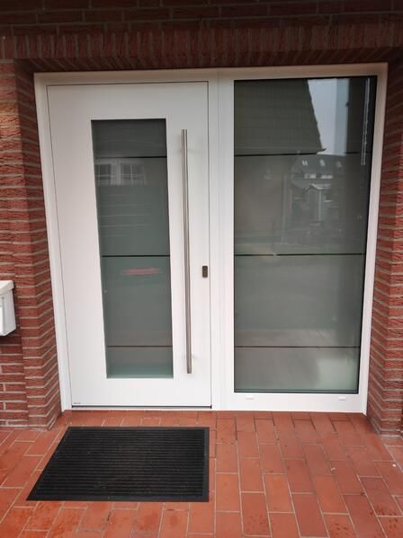 Eine weiße Tür mit einer Ziegelwand und einer schwarzen Matte davor.