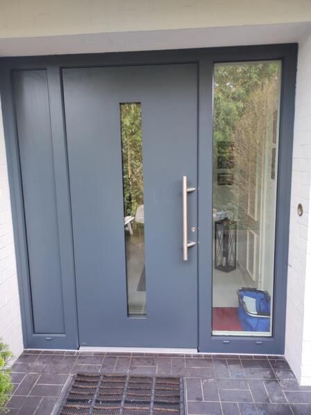 Eine graue Haustür mit Glasfenster und Edelstahlgriff.