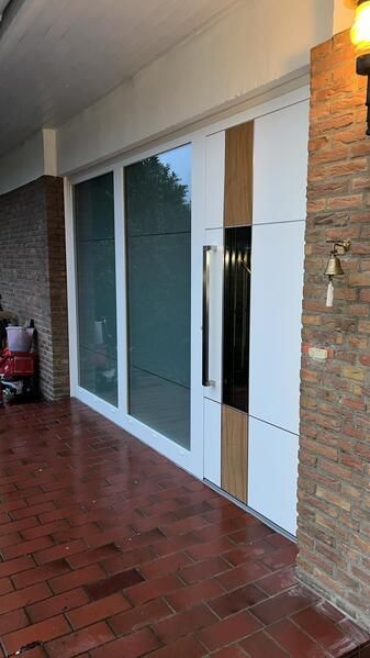 Eine weiße Tür mit einem Holzgriff steht auf einem gefliesten Boden neben einer Ziegelwand.