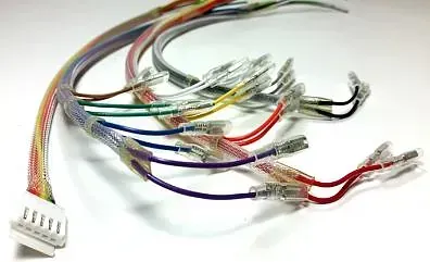 Arnés de cables con cables de varios colores, conectores transparentes y un enchufe blanco sobre una superficie blanca.