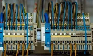 Primer plano de un panel eléctrico con numerosos cables conectados a terminales de diferentes colores, incluidos azul, amarillo y marrón.