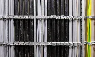 Cables organizados, principalmente negros y blancos, sujetos en su lugar por soportes metálicos dentro de un panel eléctrico.