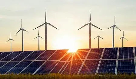 Paneles solares y turbinas eólicas recortados contra una puesta de sol, simbolizando la energía renovable.