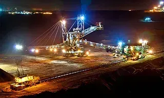 Una gran máquina minera iluminada de noche en una mina oscura y a cielo abierto. Varias luces iluminan su estructura y el terreno circundante.