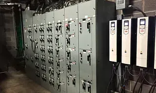 Panel de control eléctrico con varios gabinetes grises y tres variadores de frecuencia blancos en un entorno industrial.