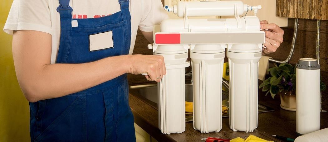 Un hombre está limpiando un filtro de agua en una cocina.