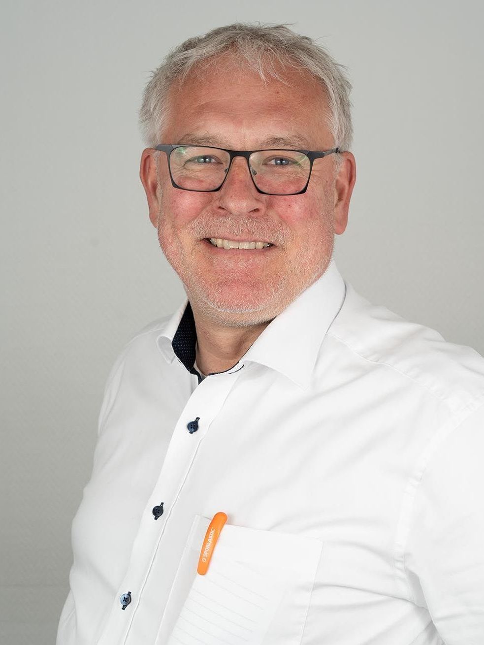 Ein Mann mit Brille und weißem Hemd lächelt in die Kamera.