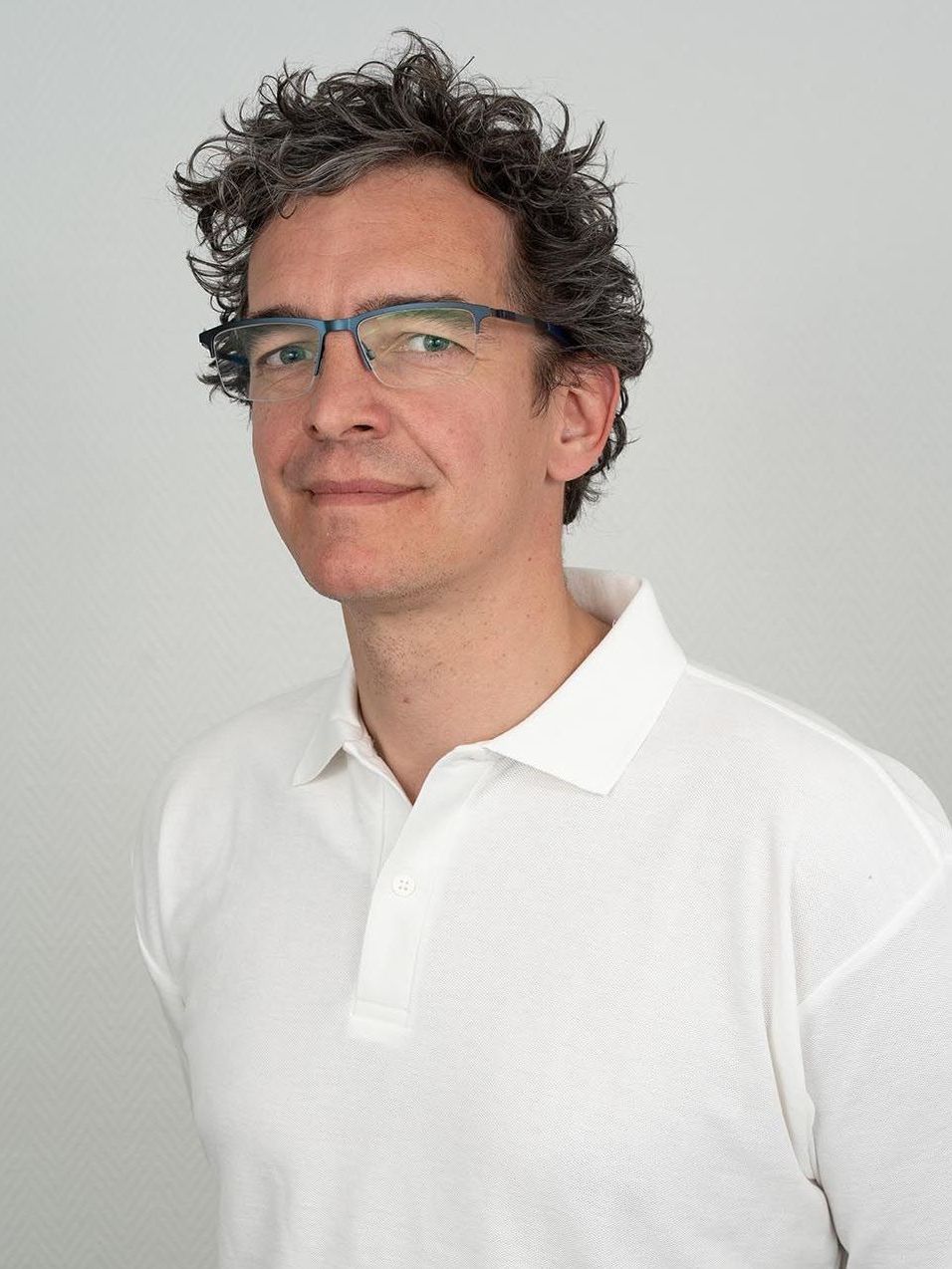 Ein Mann mit Brille und weißem Poloshirt lächelt in die Kamera.