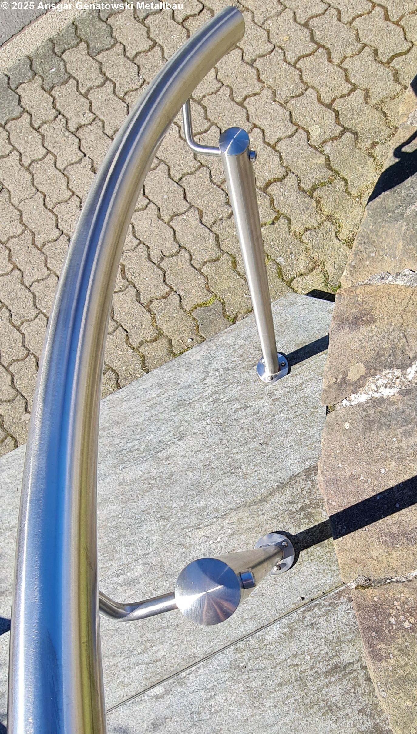 Gebogenes Geländer aus Edelstahl an einer Betontreppe.